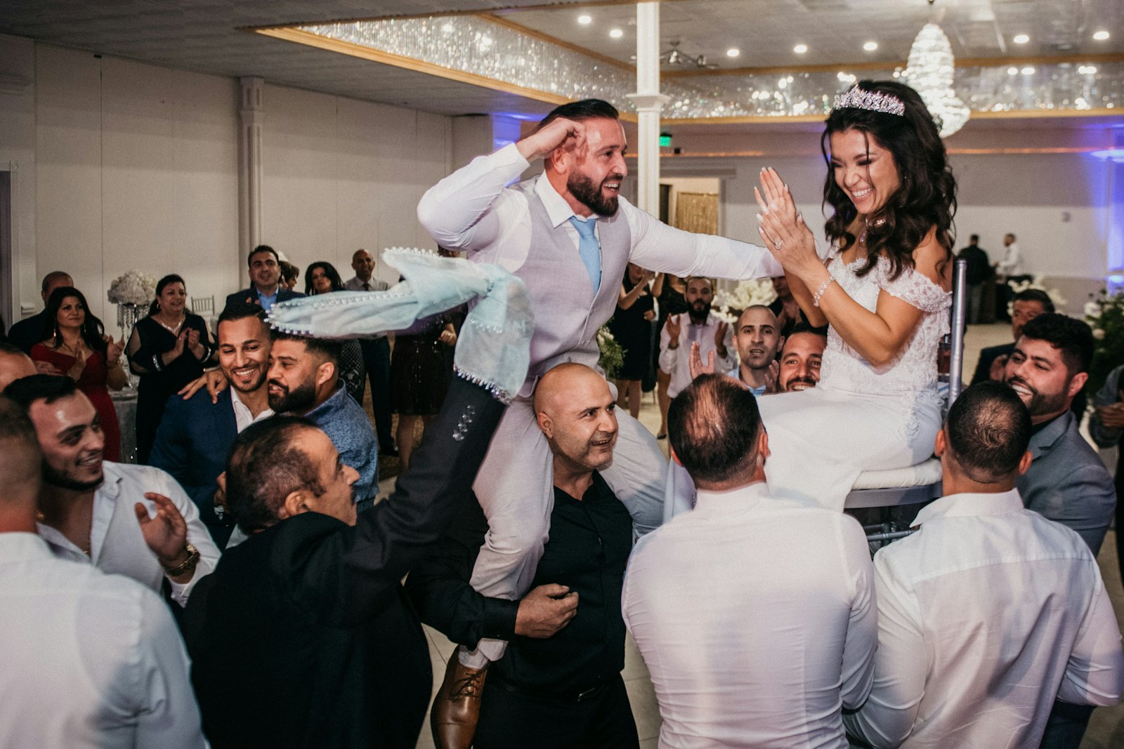 Guests lifting a bride and groom on chairs during the hora